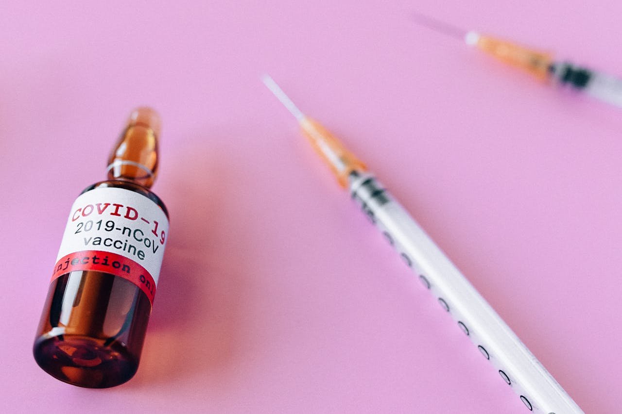 Close-up of a COVID-19 vaccine vial and syringes against a pink background, symbolizing healthcare.